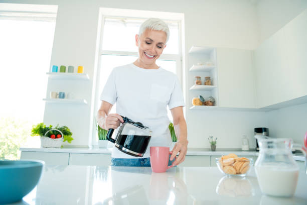 istock Charming elderly woman pouring coffee in modern kitchen with daylight 2191449248