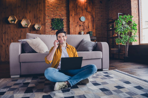 istock Young man in casual style enjoying leisure time at home while using phone and laptop in comfortable living room loft setting 2191449699