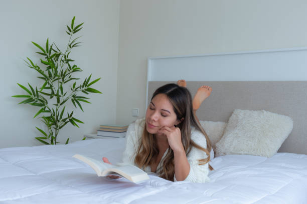 istock woman reading a book lying on a white bed in a bedroom 2191450839