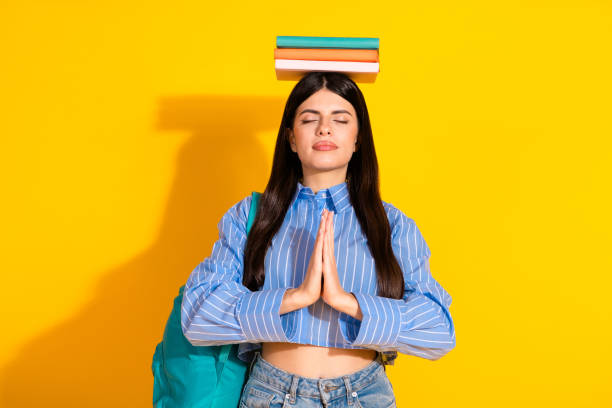 istock Relaxed student balancing books on her head against a bright yellow background 2191451018