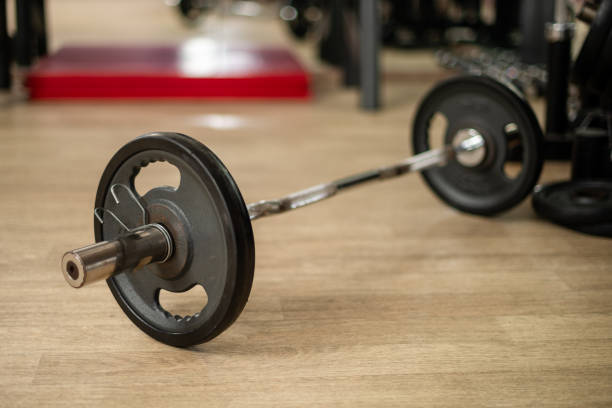 Barbell with attached weights placed on a wooden floor. Fitness equipment for weight-lifting exercises in a professional gym environment, symbolizing strength, determination and commitment to physical health.