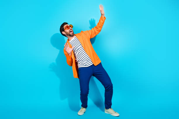 istock Charismatic young man in vibrant orange jacket posing against turquoise background, expressing joy with stylish sunglasses 2191453710