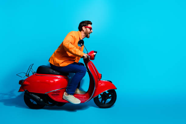 istock Dynamic young man in vibrant attire riding a stylish red scooter against a teal backdrop, exuding fun and charisma 2191453717