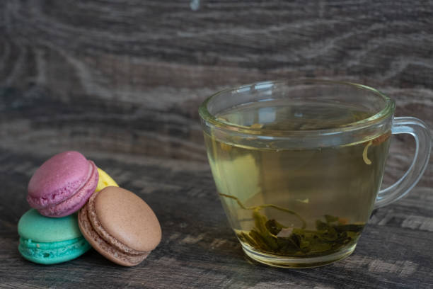 A cup of tea is sitting on a table with three macarons. The macarons are in different colors and are arranged in a row