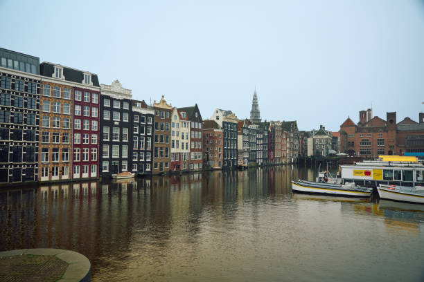 Picturesque view of colorful dutch houses lining an amsterdam canal, with boats moored alongside and a cloudy sky overhead