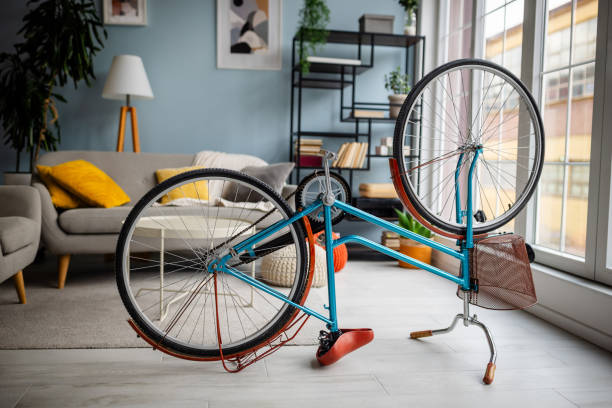 A bicycle is flipped for repairs in a modern living room featuring stylish decor and natural sunlight streaming through large windows.