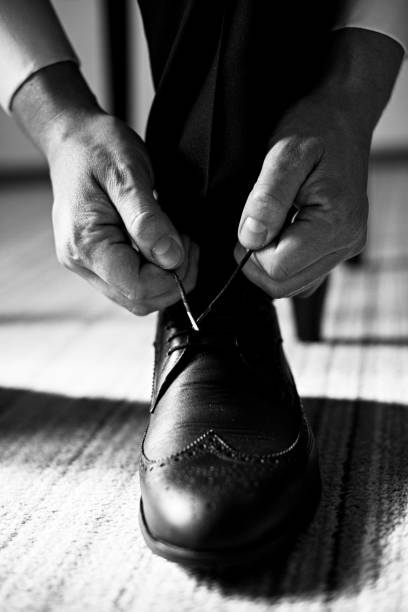 Black and white image of a person tying shoelaces on a formal shoe.
