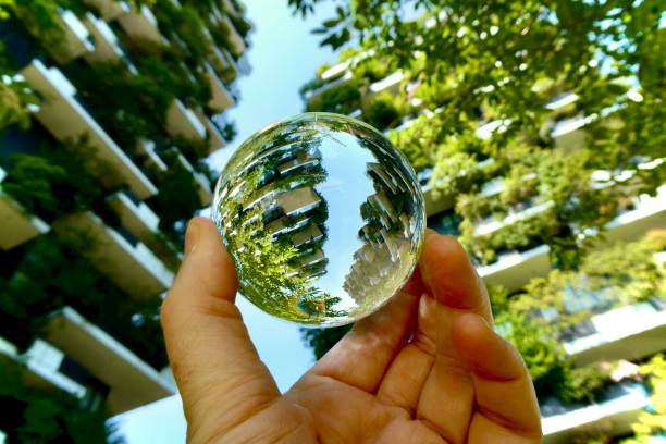 istock Hand holding crystal ball with skyscrapers background with trees on balconies 2191472279