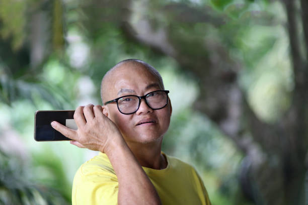 An Asian senior man is using smartphone listening to voicemail