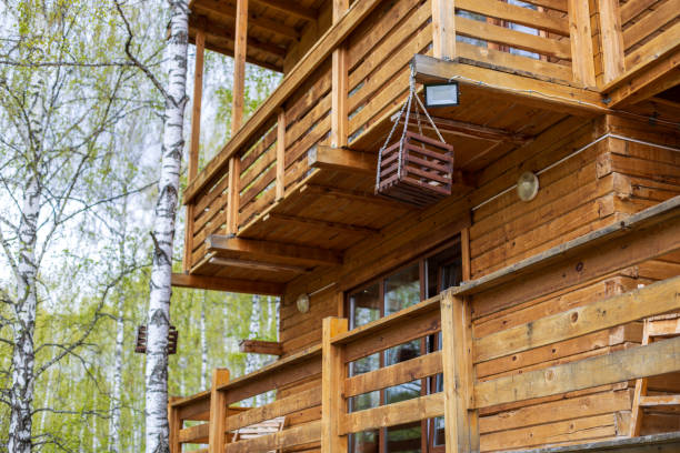 A wooden house with a balcony and a basket hanging from it. The house is surrounded by trees and has a cozy, rustic feel