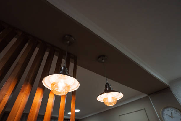 In a room adorned with wooden accents and features, two decorative lights elegantly hang from the ceiling, situated conveniently near a ticking clock that adds to the ambiance