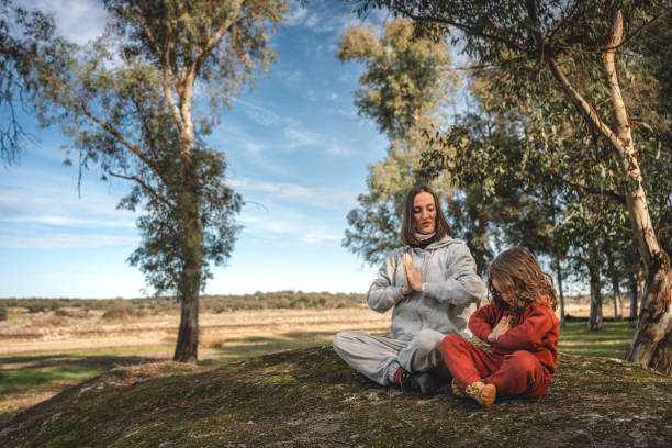 A woman and a child are sitting on a hillside, practicing yoga
