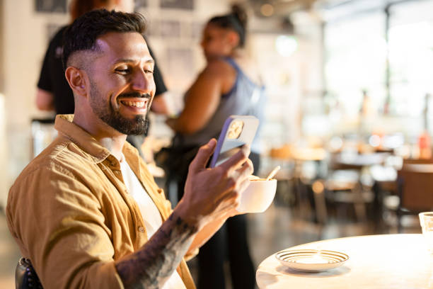 Smiling man using smartphone and drinking coffee in london cafe