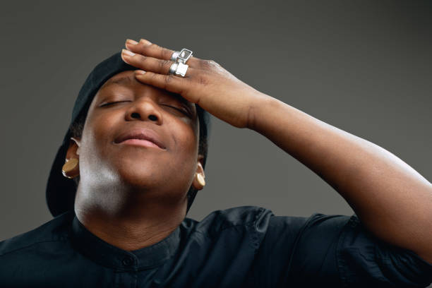 Studio portrait of a young black man wearing black shirt and cap, touching his forehead with hand and eyes closed, expressing shame or disappointment