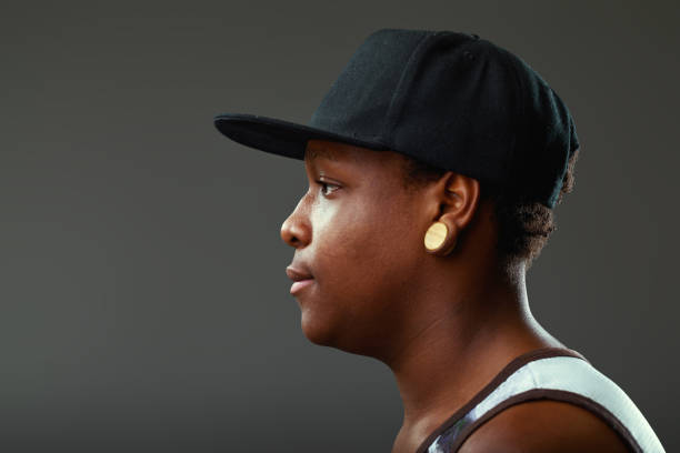 Profile of a young black woman wearing a stylish cap and a striking earring, exuding cool confidence while gazing thoughtfully away against a soft gray background