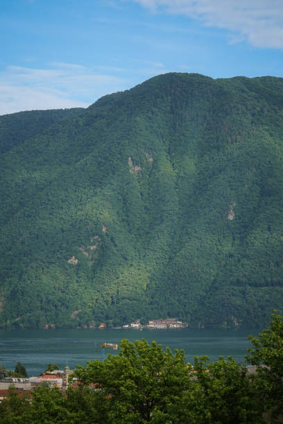 Big green forest covered mountains next to Lugano lake with few houses and a tower crane through the trees on the bottom, Lugano, Switzerland