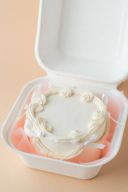 istock Delicate small lambeth style cake with white cream cheese frosting in a gift bento box. Cake as a gift for a beloved one. Spring tender cake for a woman on the beige background. Top view 2191497468
