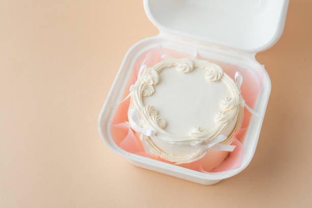 istock Delicate small lambeth style cake with white cream cheese frosting in a gift bento box. Cake as a gift for a beloved one. Spring tender cake for a woman on the beige background. Top view 2191497474