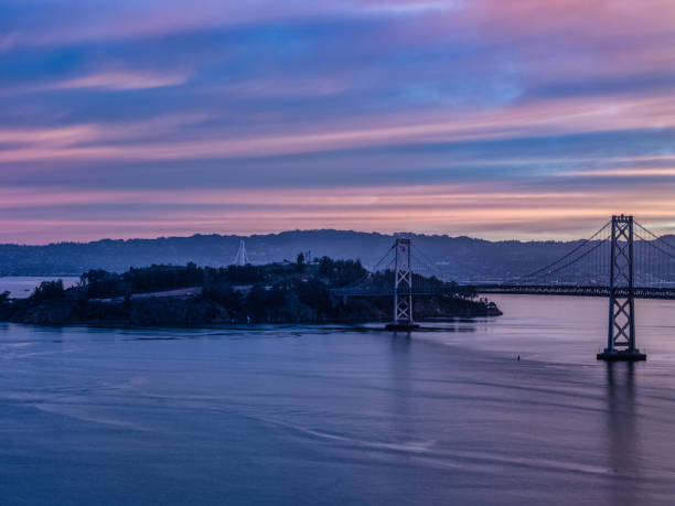 Aerial View of Yerba Buena Island across the bay at sunrise cast in shades of blue. Bay Bridge in foreground.