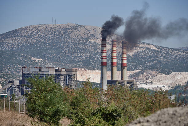 Industrial plant with chimneys releasing smoke pollution, visible among a mountainous landscape, illustrating environmental challenges and contrasting natural scenery.