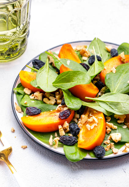 istock Wintervegan persimmon salad with walnuts, blue raisin and spinach, white background, top view 2191518821