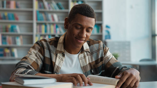 African American man bookworm reader library reading book smiling leisure student learning educational studying intelligence pleasure male guy smart literature page engaged textbook college exam novel