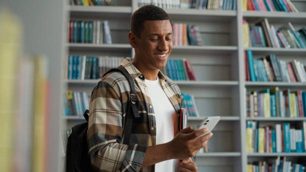 istock African American man guy user mobile phone smartphone cellphone network student study educational bookcase bookstore library internet wifi online university archive high school browser literature male 2191528407