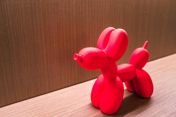 This image features an intricately twisted red balloon dog, showcasing the art of balloon sculpting. The dog is positioned on a wooden surface, with its vibrant red color providing a striking contrast to the wood's natural tones. The sculpture's form is both whimsical and lifelike, demonstrating the skill involved in transforming a simple balloon into a recognizable and endearing figure.
