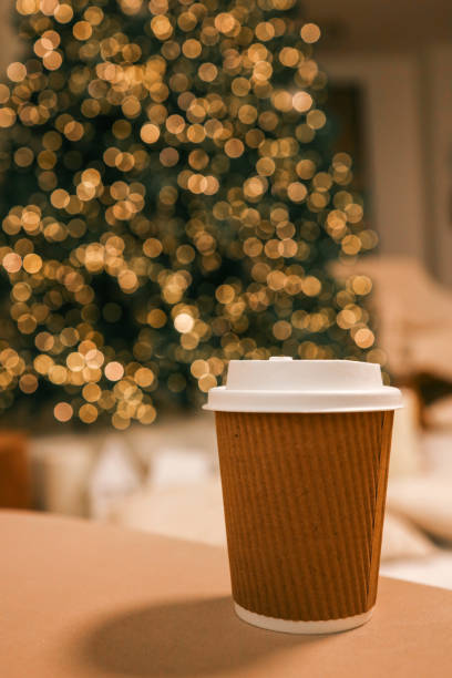 istock Takeaway coffee cup in eco-friendly brown paper holder with white lid, placed on a soft background with Christmas tree bokeh lights. Perfect for festive, cozy, and eco-conscious themes 2191545114