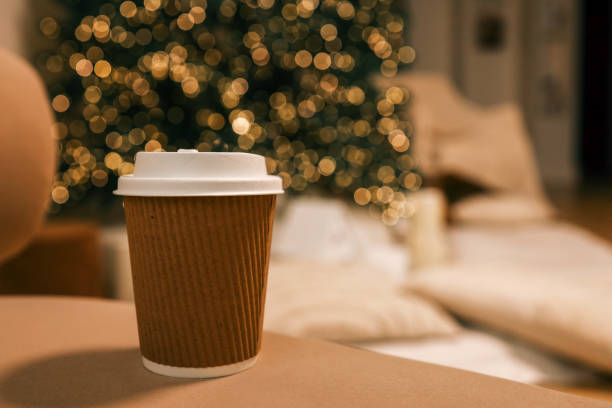 istock Takeaway coffee cup in eco-friendly brown paper holder with white lid, placed on a soft background with Christmas tree bokeh lights. Perfect for festive, cozy, and eco-conscious themes 2191545116