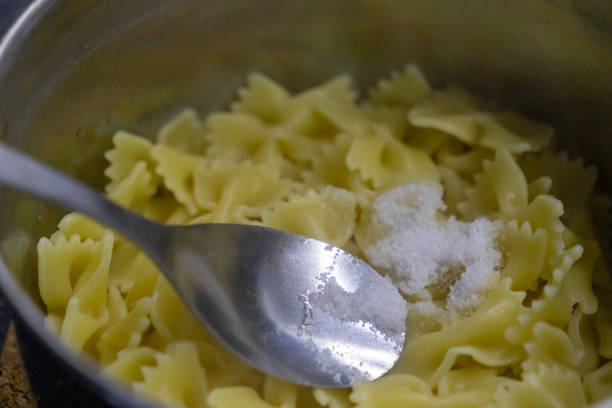 istock Adding salt to freshly cooked farfalle pasta in a metal pot with a spoon 2191546064