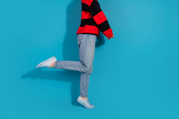 A stylish young woman wearing a striped red jumper and casual jeans, standing against a vibrant blue background, expressing charm and modern elegance.