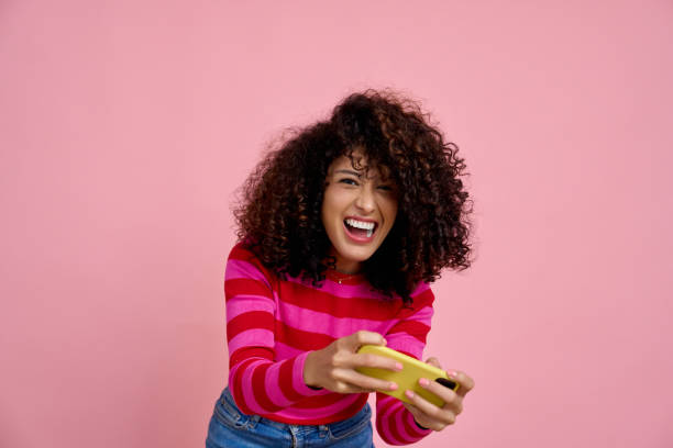 istock Excited young woman playing mobile game on pink background 2191548415