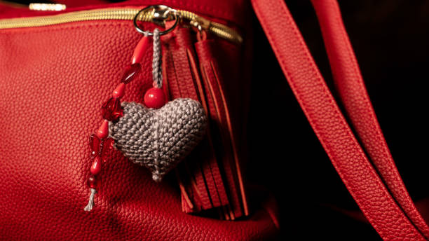 Gray crochet heart keychain hangs on a red handbag.