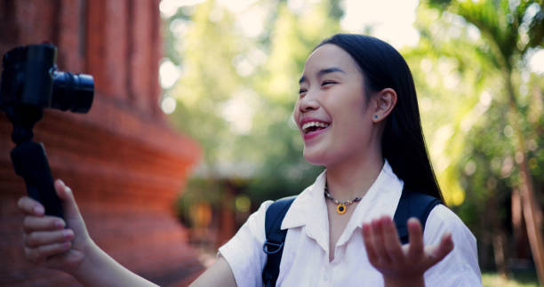 Portrait of Asian female tourist having fun records content using a camera attached to a selfie stick, explaining the history of the ancient site to viewers.