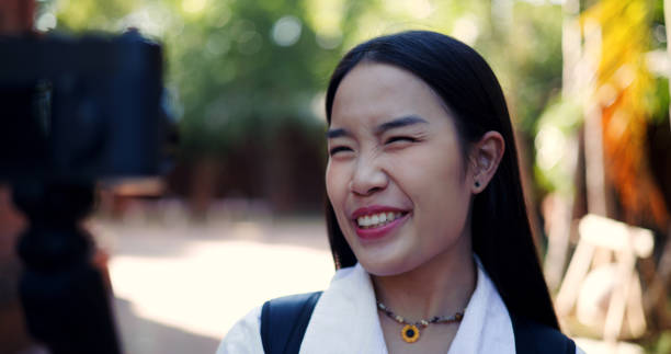 Selective focus shot, Asian female tourist having fun records content using a camera attached to a selfie stick, explaining the history of the ancient site to viewers.
