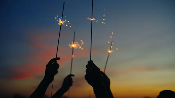 istock Silhouetted Hands Raise Glowing Golden Sparklers Into Twilight Summer Sky 2191560335