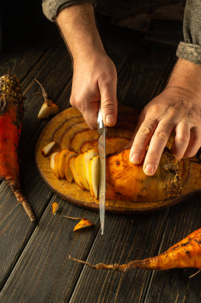 istock A close-up view captures hands meticulously cutting into a bright orange beet vegetable, surrounded by fresh produce on a textured wooden surface, evoking a sense of culinary artistry 2191563356