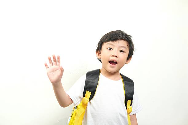 A young boy in a white shirt and yellow backpack, waving with a cheerful expression. Perfect for back-to-school promotions, educational content, kid-friendly advertisements, and classroom materials
