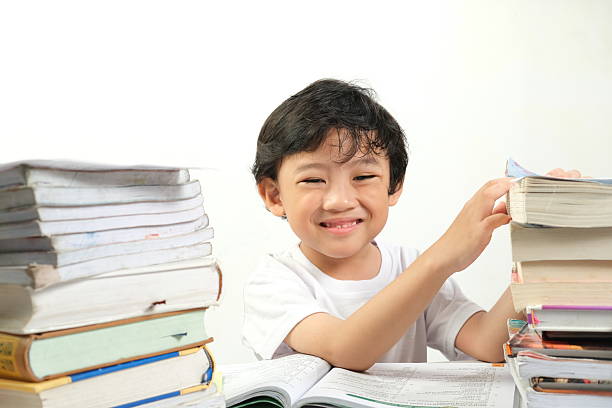 A cheerful young boy studying surrounded by stacks of books, smiling brightly. This image is perfect for educational materials, school promotions, tutoring services, and academic websites.