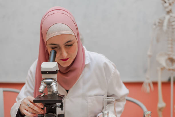 istock A female Muslim scientist doing science research looking through a microscope in the lab. 2191565761
