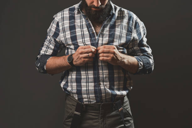 Young handsome man posing in the studio in front of a gray wall. Cap, plaid shirt, beard, hipster style.