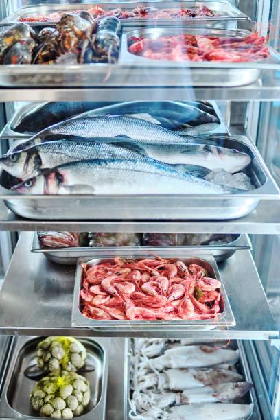 Small business owner - African American man holding tray of raw shrimp by display of fresh fish on ice