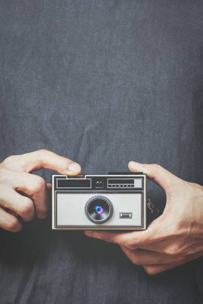 close up male hands holding retro camera and pressing shutter button on black shirt background