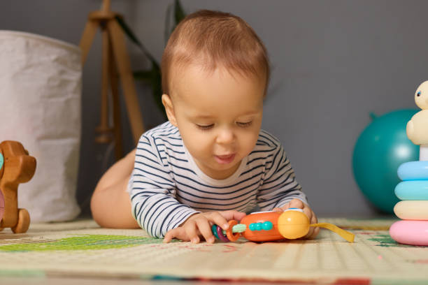 istock A young child is focused on a bright, colorful toy while lying on their stomach on a soft mat in a sunlit room. The atmosphere is cheerful and playful, perfect for exploration 2191578749