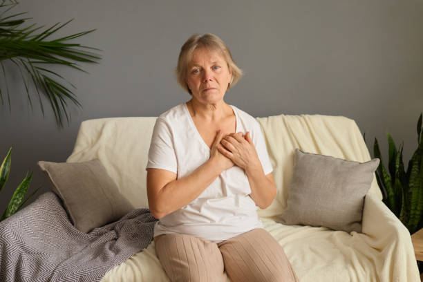 istock An older woman sits on a comfortable sofa, showing concern as she holds her chest. Soft natural light fills the room, suggesting a calm atmosphere despite her distress 2191578920