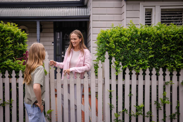 istock Mother and daughter chat over white picket fence 2191579782