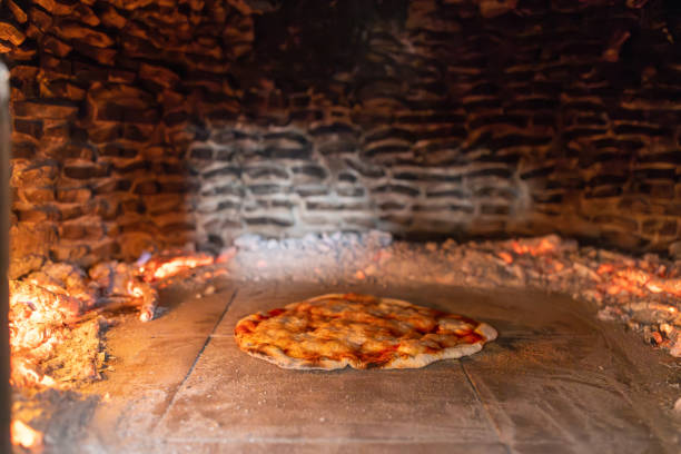 A freshly prepared pizza baking in a traditional wood-fired oven in a rustic pizzeria. The glowing embers and authentic stone interior create a warm and inviting atmosphere, perfect for showcasing artisanal pizza-making techniques.