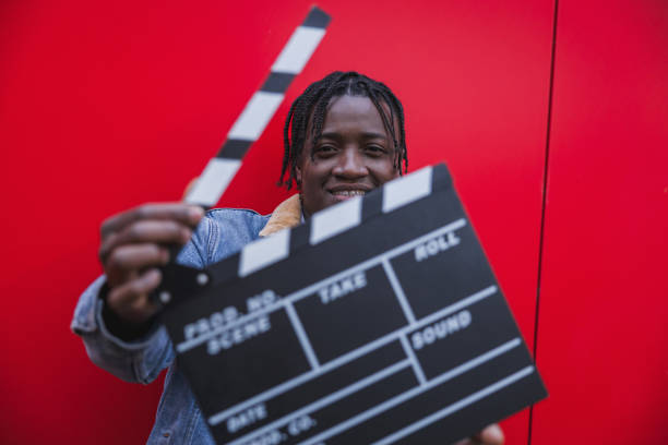 Young filmmaker portrait smiling and holding a clapperboard on red background, ready to start filming.