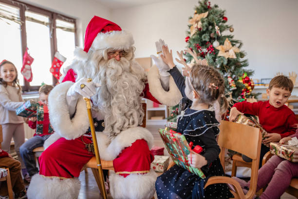 A delightful holiday moment as Santa Claus shares a joyful high-five with a young girl, surrounded by children, Christmas gifts, and cheerful decor in a festive setting.